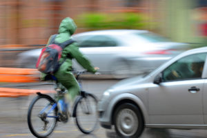 Person in green rain jacket riding a bike in front of a car